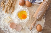 top view eggs, dough, flour and rolling-pin on wooden table background